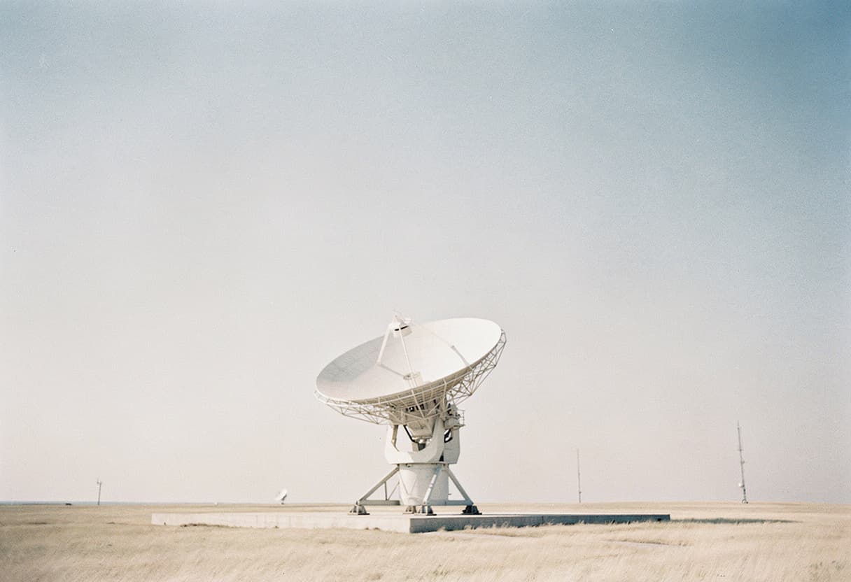 A lone radio telescope dish on open grassland under a pale sky