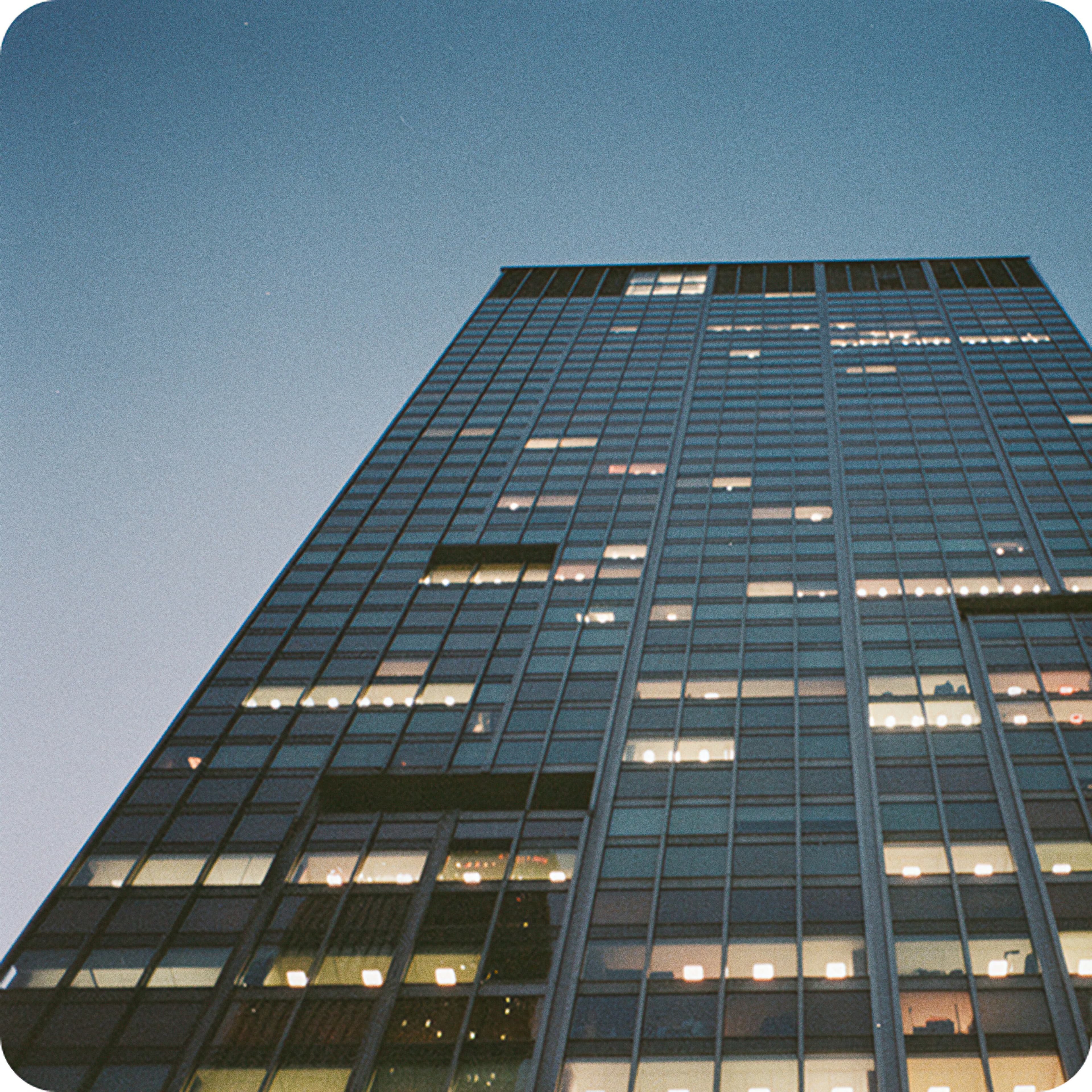 Glass office tower at dusk with lit windows, representing financial services